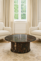 Round wooden coffee table in a living room with beige chairs and large windows.